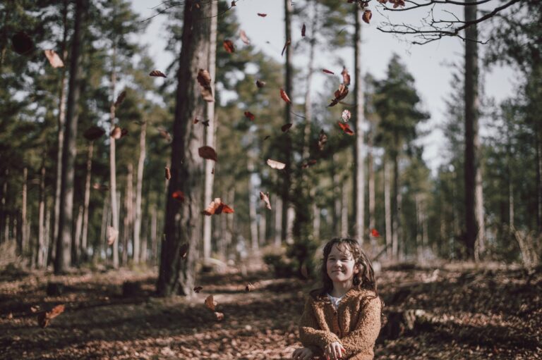 Fetiță care se joacă cu frunze de toamnă în pădure în vacanța de toamnă
